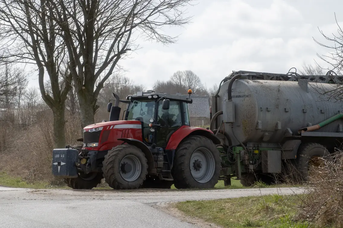 Tracteur rouge tractant une tonne à eau sur une route de campagne