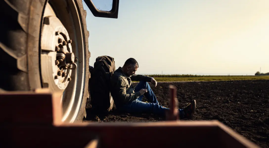 Deux agriculteurs assis au pied d’un tracteur, au coucher du soleil