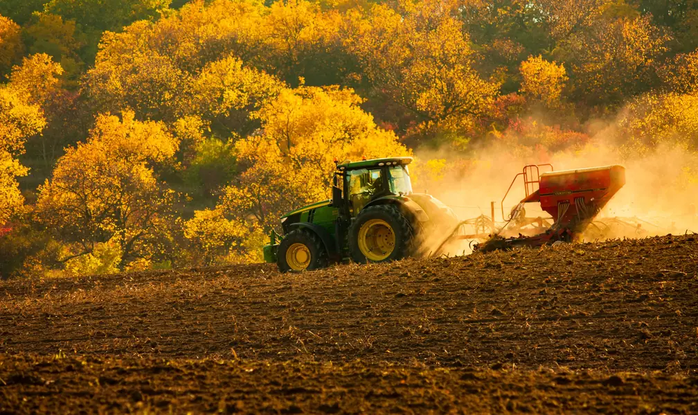 Tracteur vert épandant dans un champ, feuillage d’automne en arrière-plan