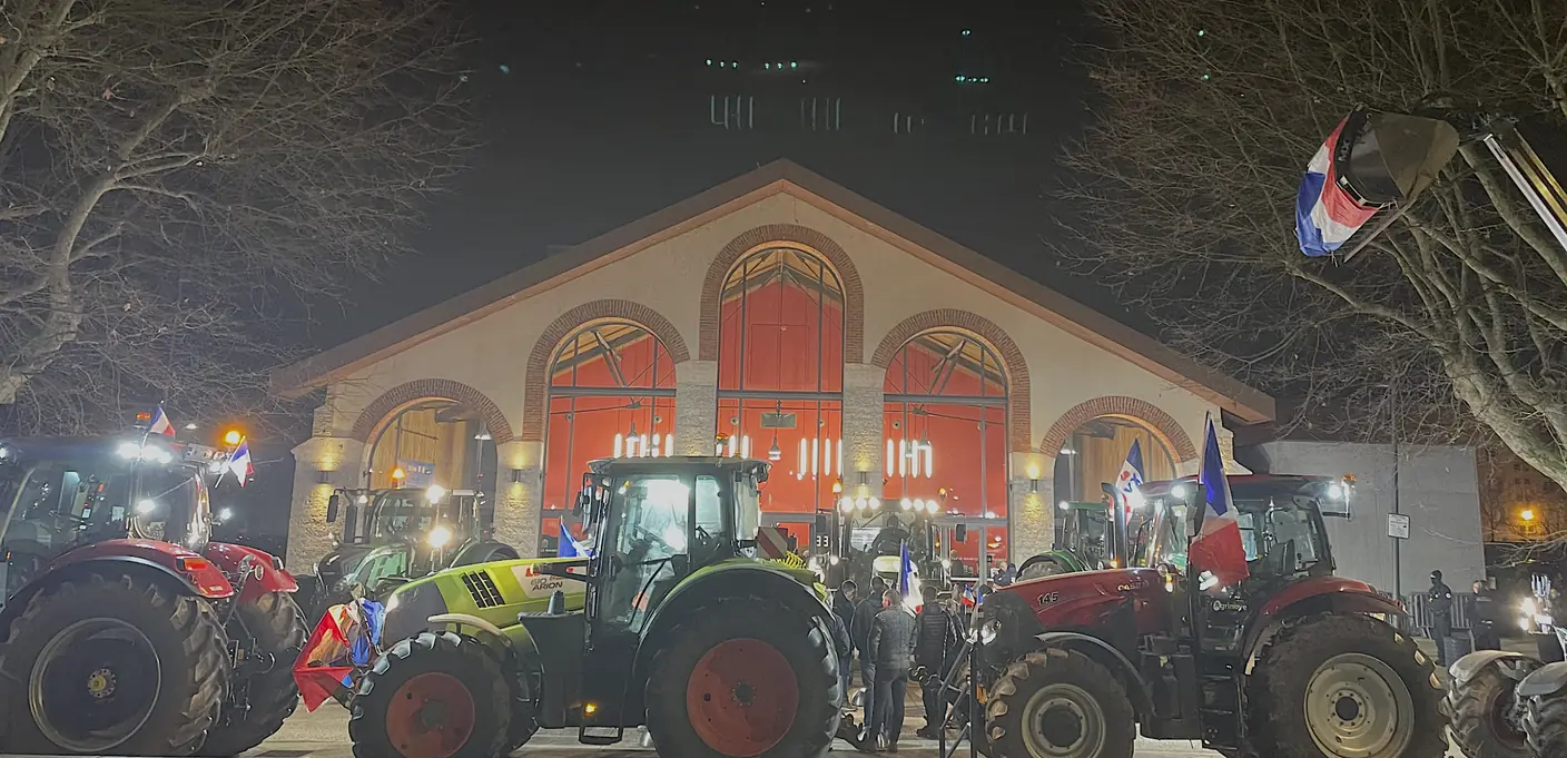 Tracteurs rassemblés devant un bâtiment illuminé lors de la mobilisation à Vienne